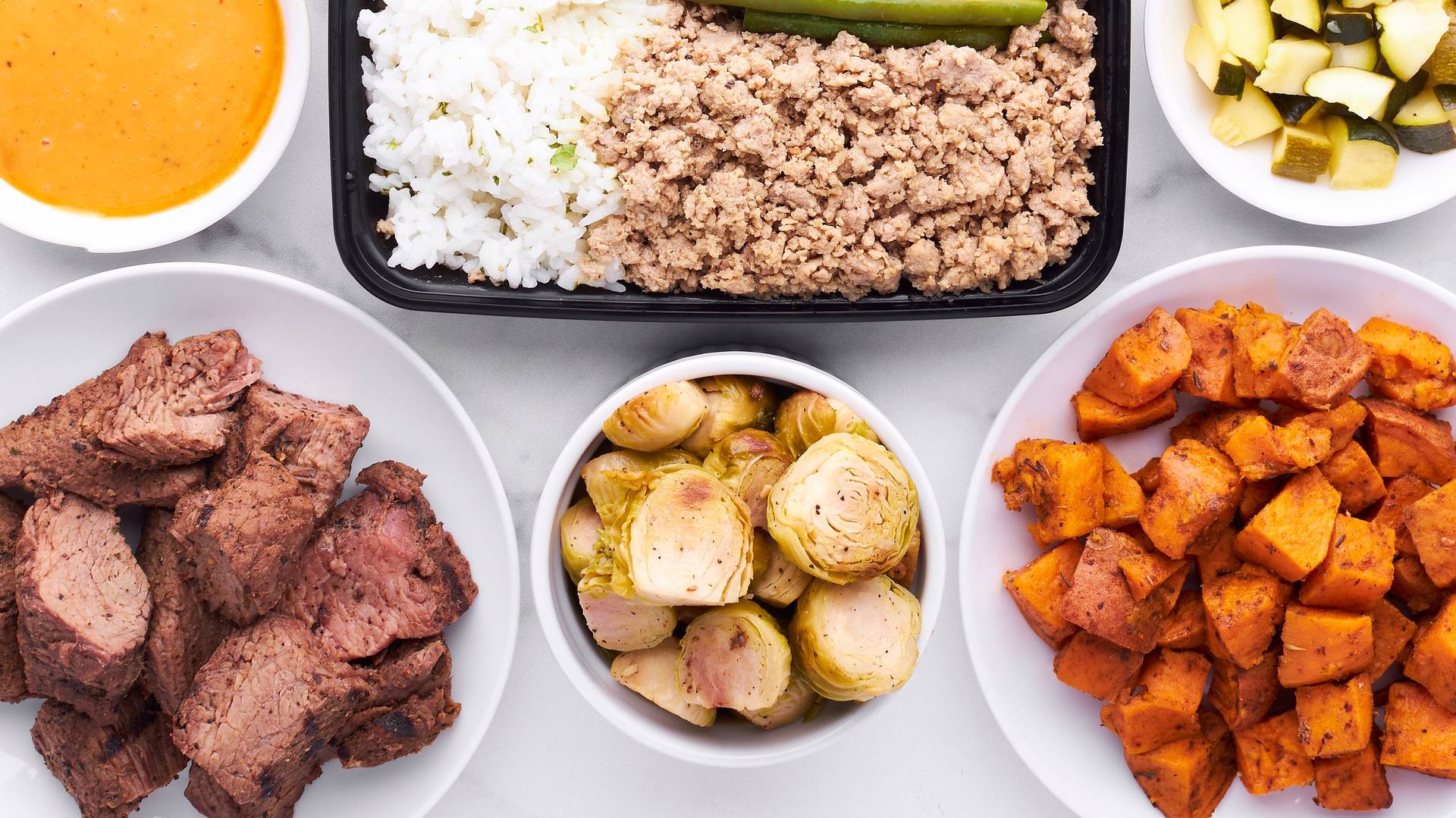 Separately prepped components — rice, ground meat, roasted vegetables, sauce — in bowls ready to be mixed into different dinners